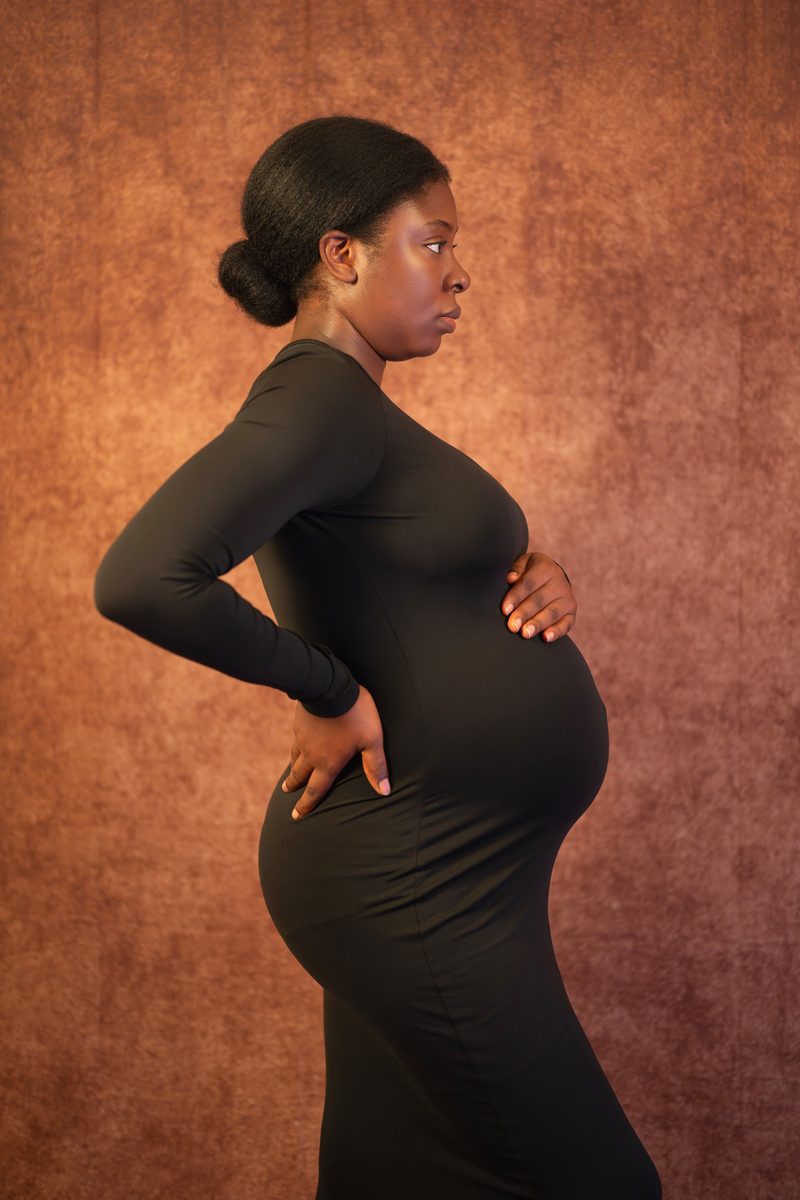 Maternity portrait in profile, black dress on a painted backdrop