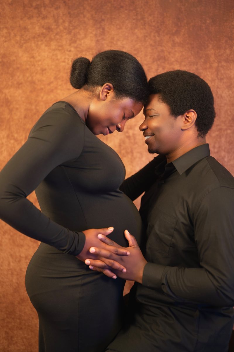 Expecting couple forehead to forehead on a painted backdrop