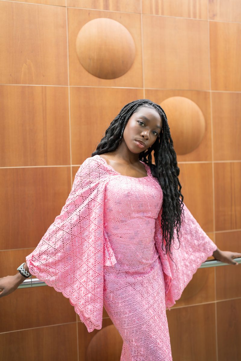 Pink lace sleeves spread against a warm wood wall