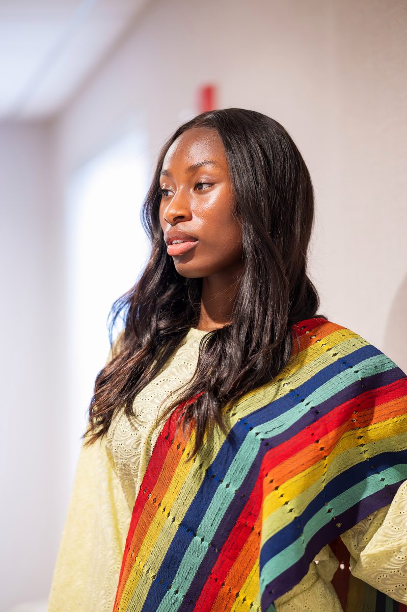 Woven rainbow kente shawl over a pale yellow dress