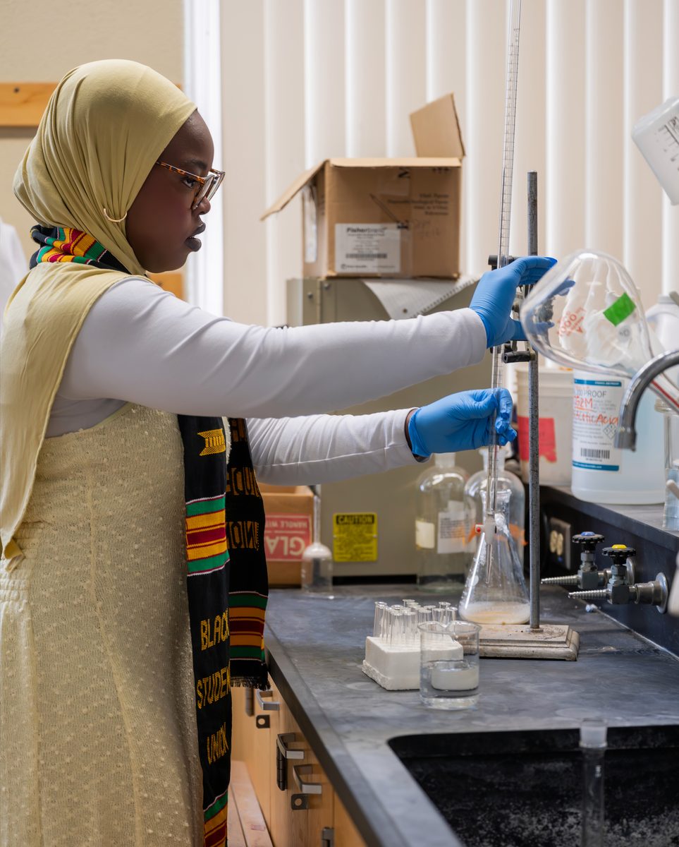 Graduate pouring a flask at a lab bench