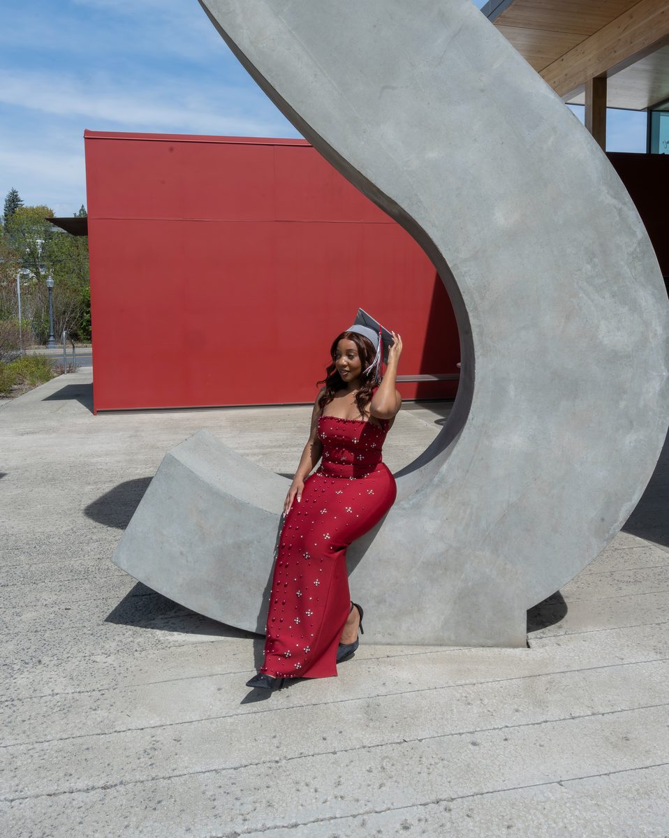 Graduate in a red gown, seated in a giant concrete letter