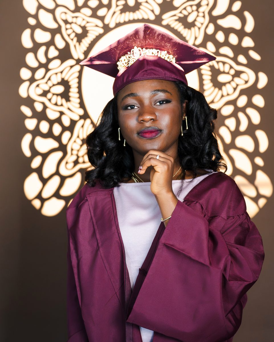 Maroon gown and crowned cap before a gold light pattern