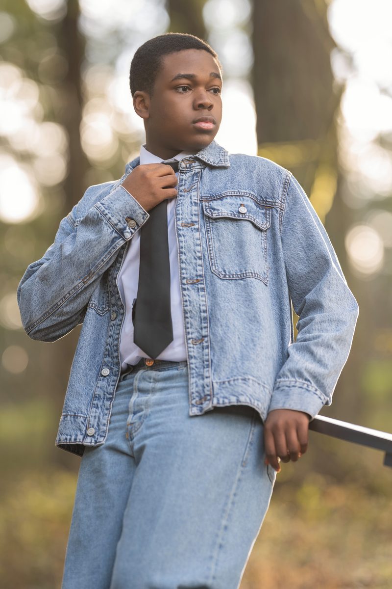 Denim jacket and tie, standing by a rail in the forest