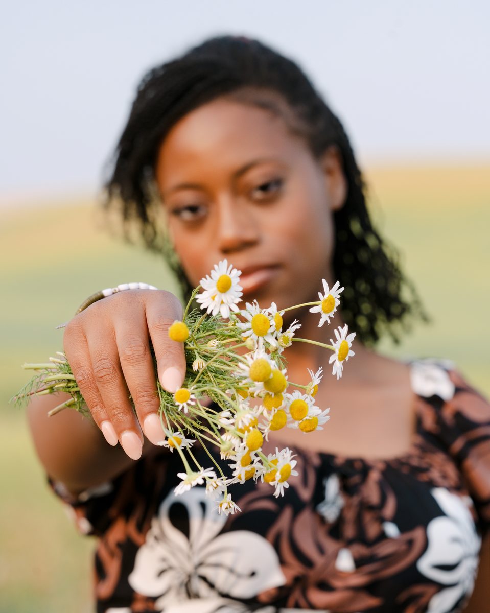 Holding out wild daisies toward the lens in a wheat field