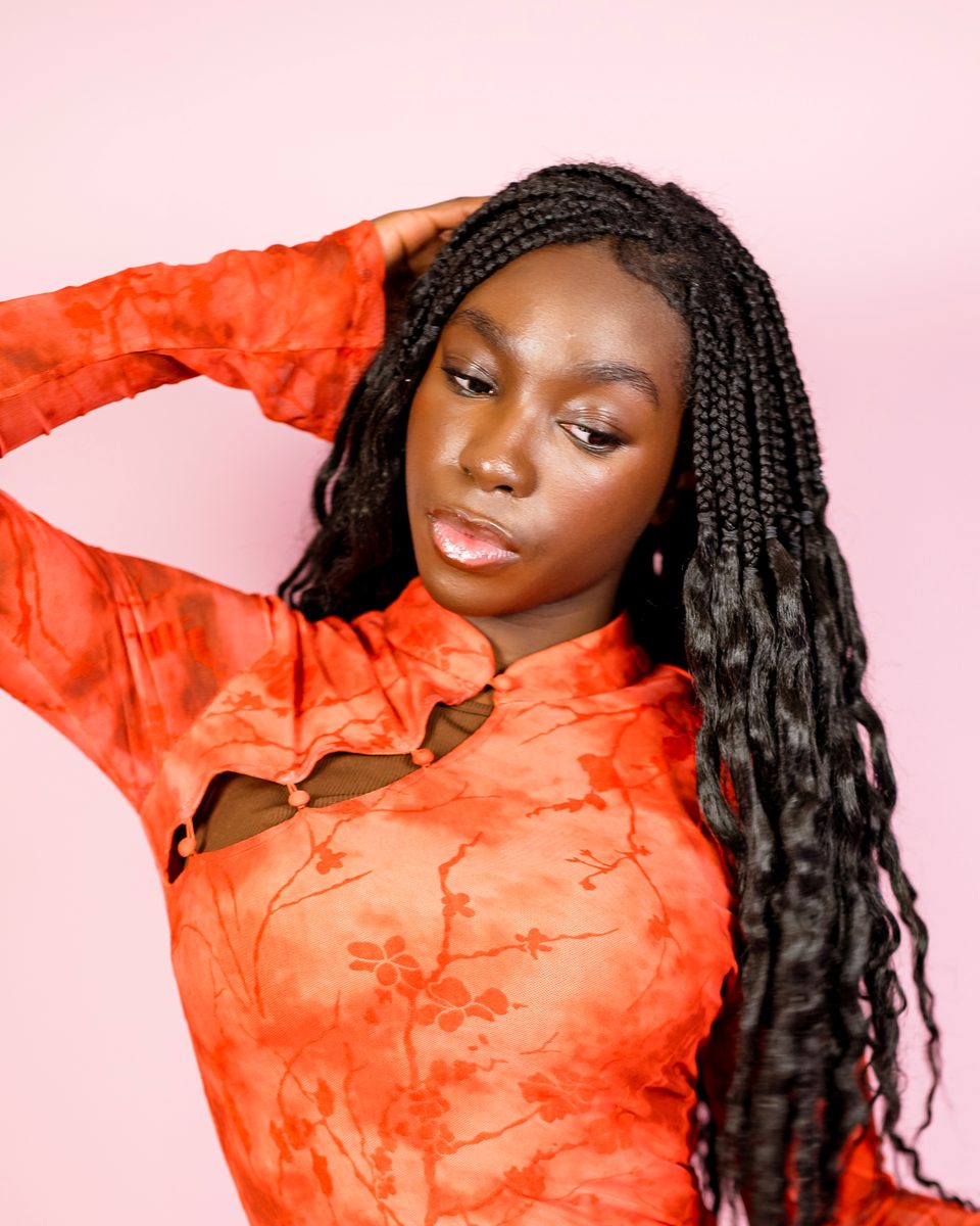 Coral dress, arm over her head, pink backdrop