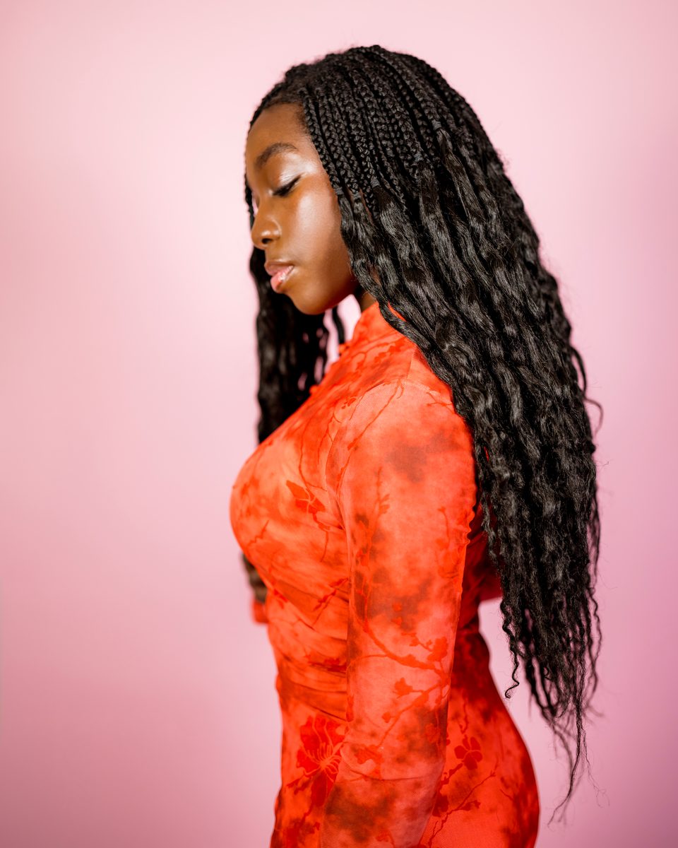 Coral dress in profile, eyes lowered, pink backdrop