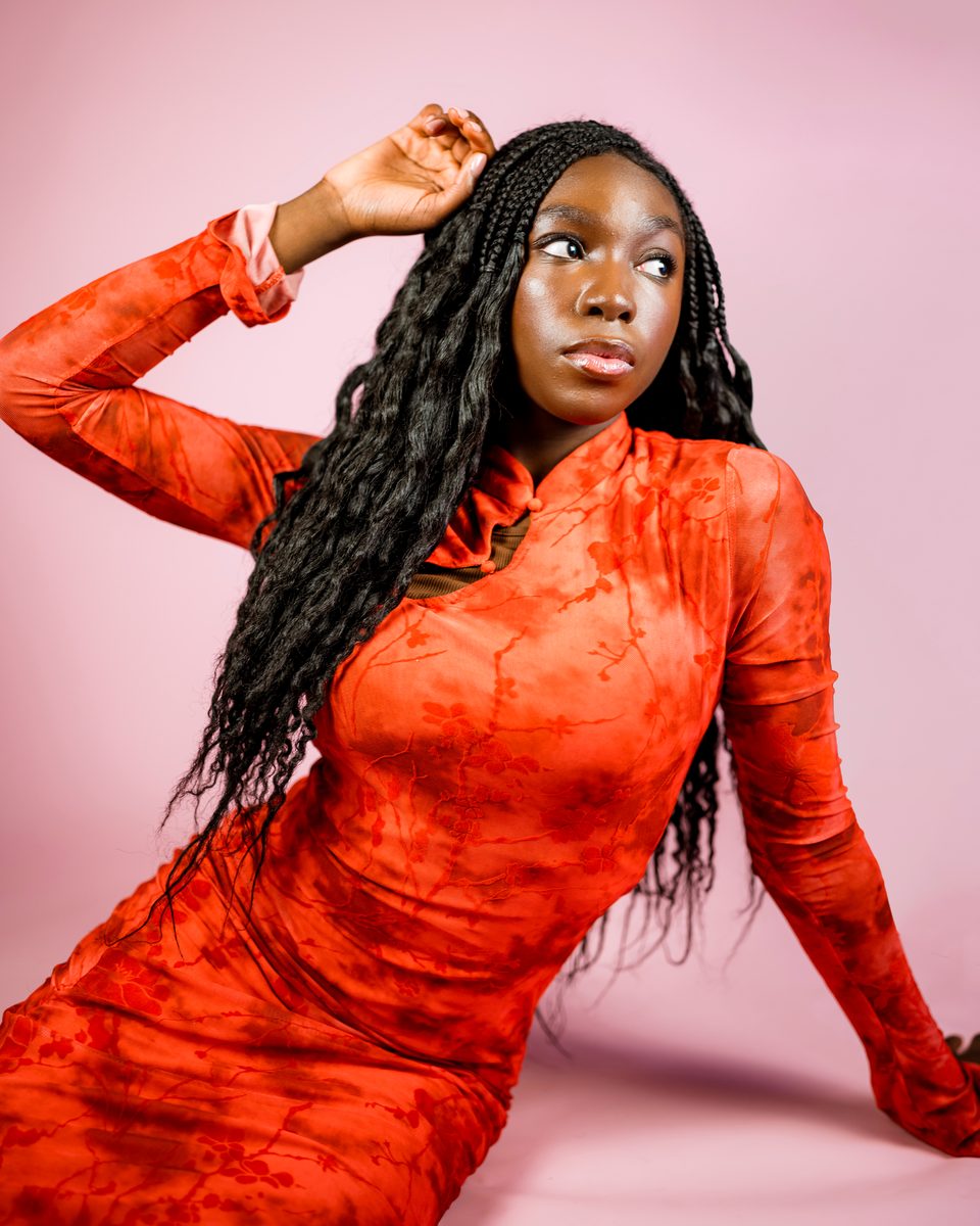Coral dress on a pink backdrop, arm raised