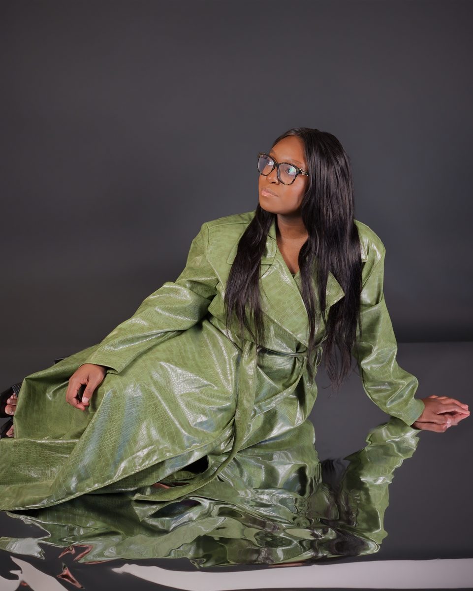 Olive leather coat, seated on a reflective black floor