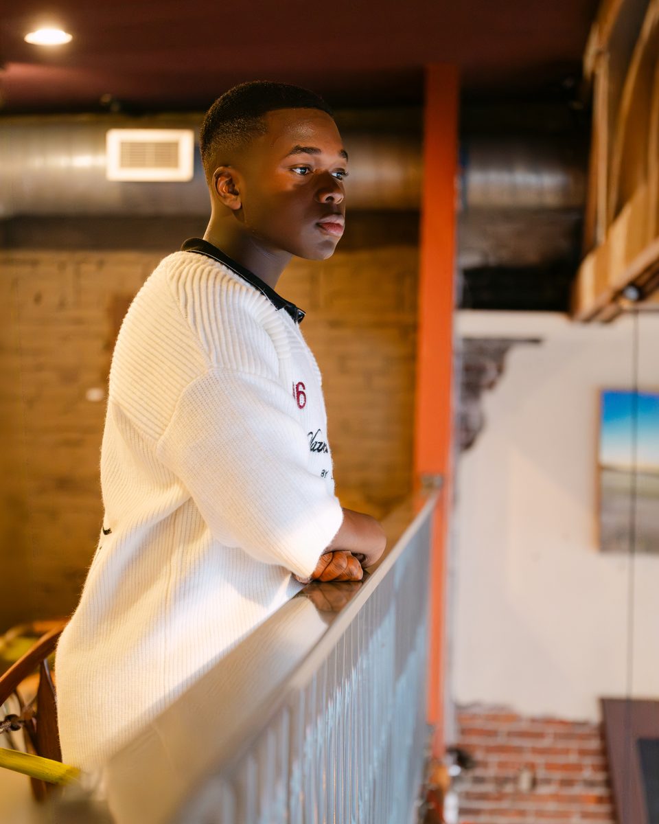 Knit polo, leaning on a rail inside a coffee shop